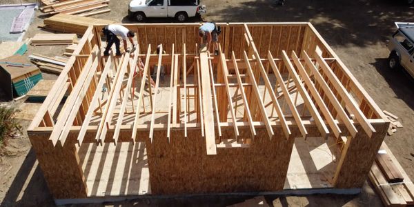 Construction workers framing wooden roof beams on a building under construction.