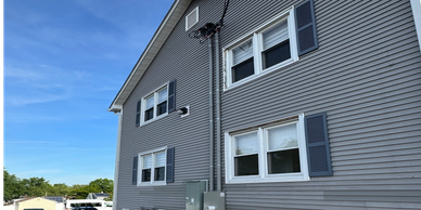 Gray residential building with multiple windows and parked cars outside.