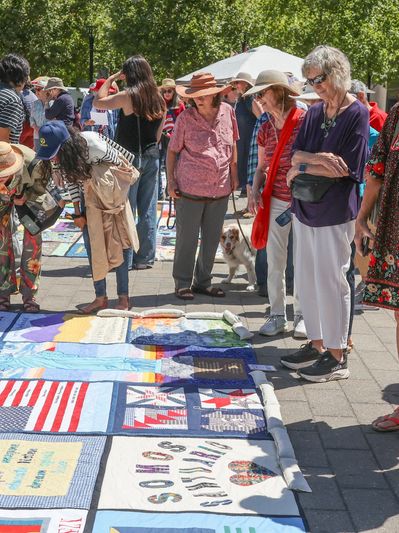 people standing around a quilt laying on the ground at an event