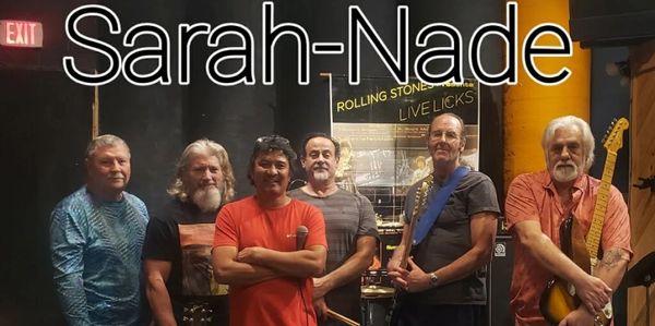Six men posing as the band Sarah-Nade in a music studio with instruments.