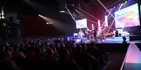 A live band performs on stage in front of a seated audience at a concert.