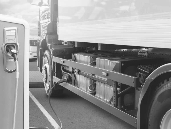 An electric truck is charging at a station, showing its battery pack.