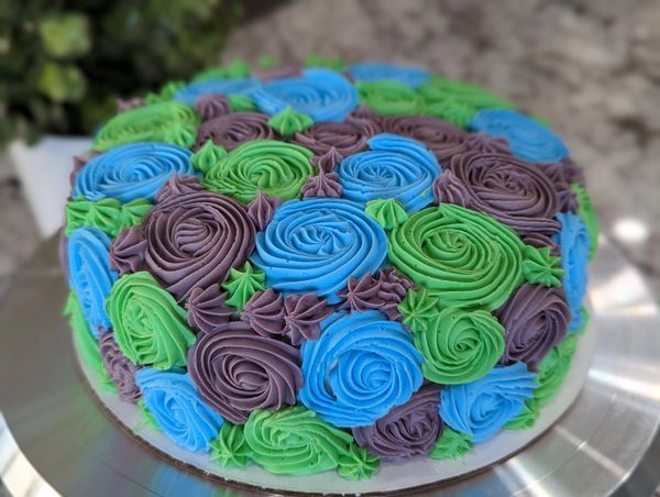 8-inch cake, vanilla frosting in blue, purple & green rosettes covering top and sides