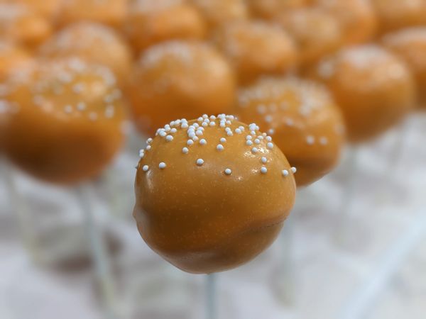 Pumpkin spice cake pop, vanilla candy coating in orange, white nonpareils
