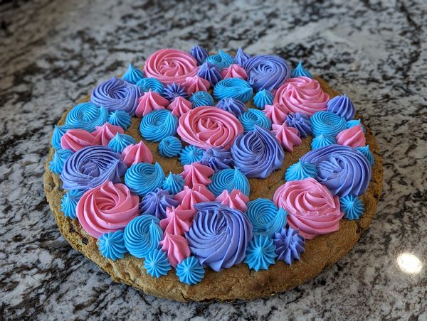 Giant chocolate chip cookie, vanilla frosting in pink, blue, and lavender