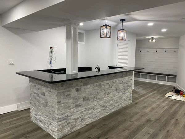 Modern basement bar with stone facade and black countertop under pendant lights.