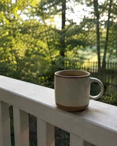 Coffee mug on a porch railing with a green forest background.