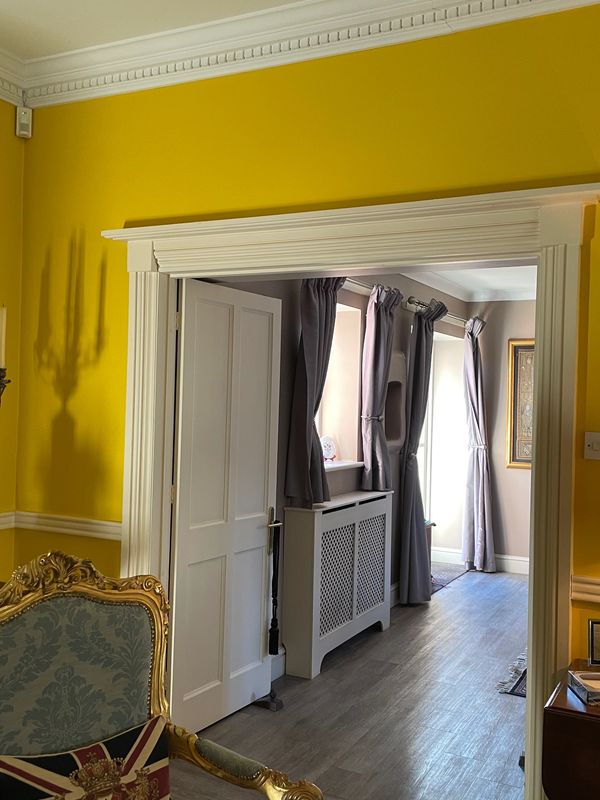 Elegant room with bright yellow walls, classic chair, and open door leading to a curtain-lined hallway.