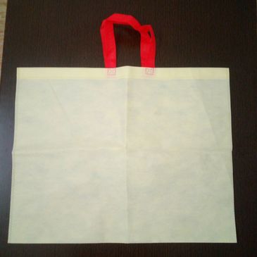 A plain white reusable bag with red handles on a dark surface.