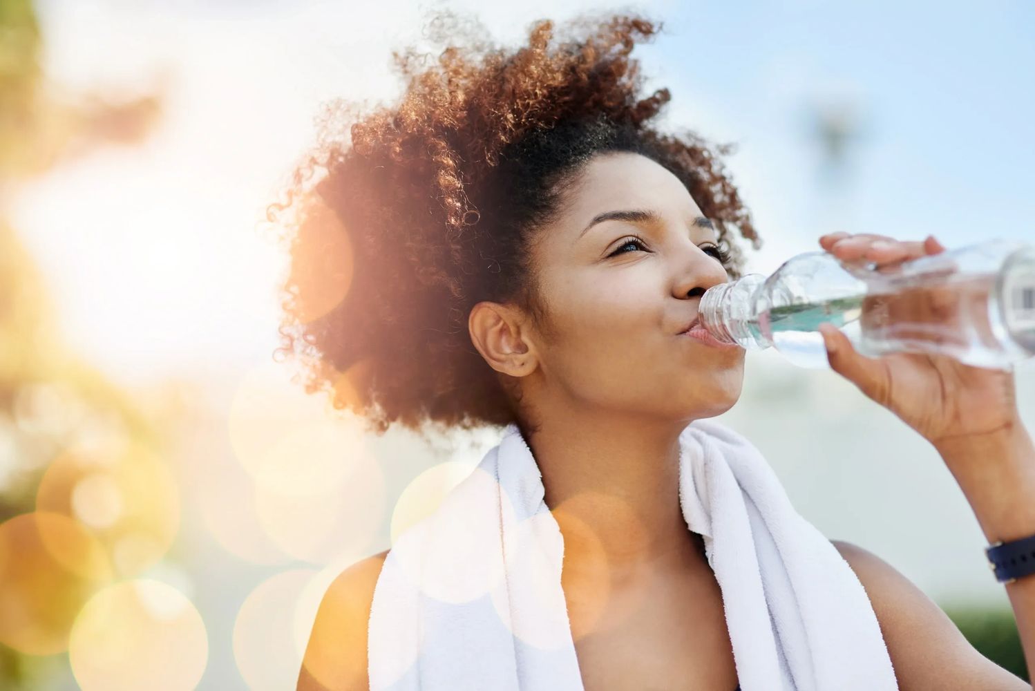 Woman drinking water with Abstinal™ outdoors with a towel around her neck.