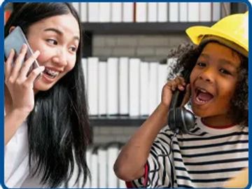 Two girls happily talking on phones, one wearing a construction helmet.