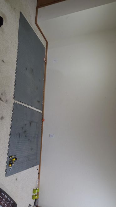 Messy workout area with black rubber mats and scattered tools and dumbbells.