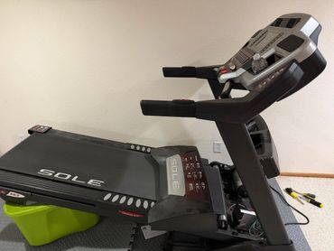 A partially disassembled Sole treadmill with tools nearby on a foam floor mat.