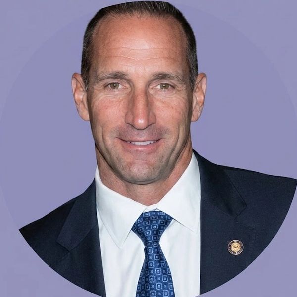 Portrait of a man in a suit and tie with a purple background.