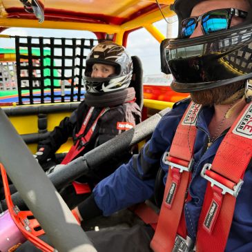 Two race car drivers inside a rally car wearing helmets and safety gear.