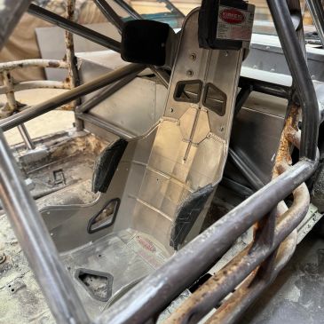 Bare metal racing seat inside a stripped race car with roll cage.