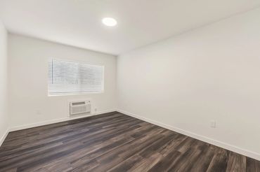 Empty room with white walls and dark wooden flooring.