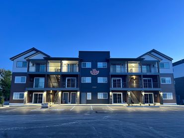Modern three-story apartment building illuminated at dusk.