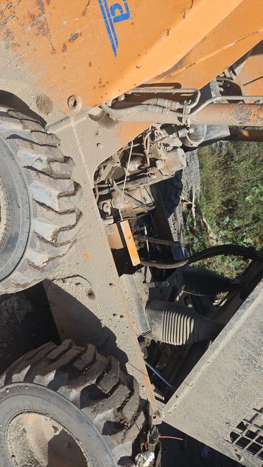 Close-up of a dusty, rugged construction vehicle's tire and mechanical parts.