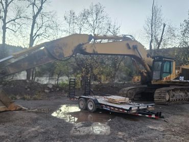A large CAT excavator parked near a flatbed trailer on a muddy ground.
