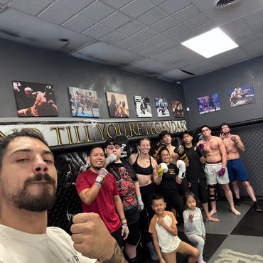 Group of diverse people in boxing gloves posing inside a gym with fight photos on the wall.