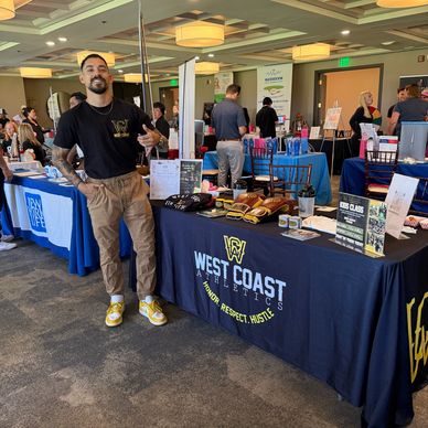 Man standing at a West Coast Athletics promotional booth at an indoor event.