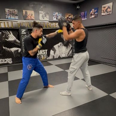 Two men sparring in an MMA gym with gloves and pads.