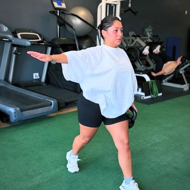 Woman exercises with a kettlebell at the gym, balancing with one arm extended.