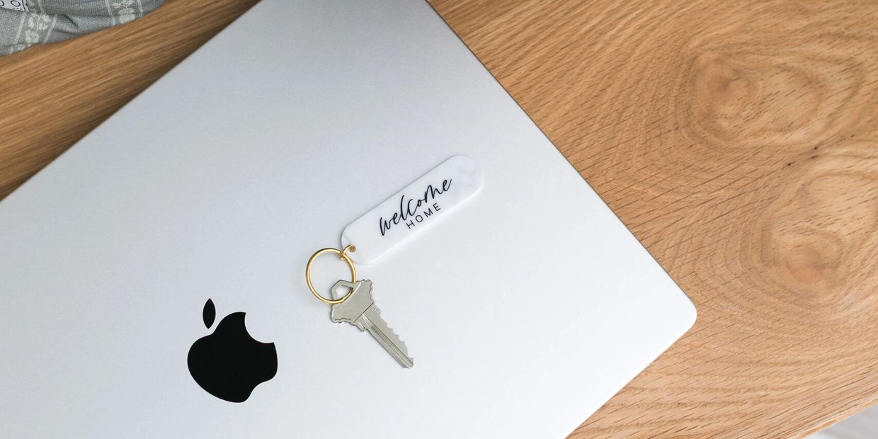 MacBook laptop on wood desk with a "Welcome Home" house key - Delia Hines relocation specialist help