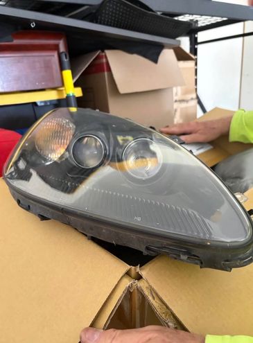Car headlight assembly placed on a cardboard box with hands nearby.