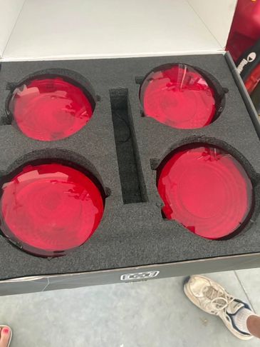 Set of four red circular lenses in foam packaging inside a box.