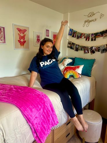 Freshman college girl proudly sitting on bed on move in day