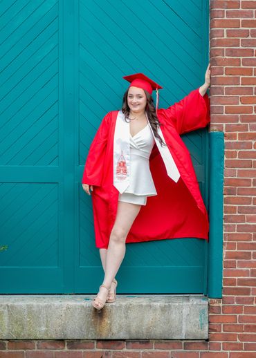 high school girl in cap and gown standing next to brick building