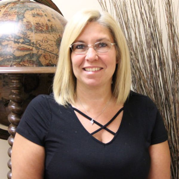 Smiling woman with blonde hair and glasses in a black top, standing indoors.
