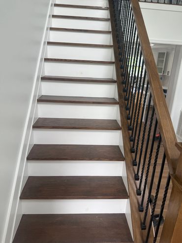 Wooden stairs with white risers and black iron balusters in a modern home.