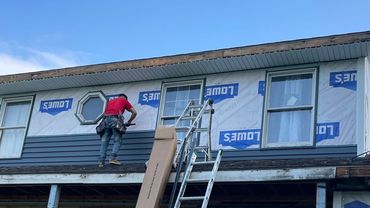 Worker installing siding on a two-story house under renovation.