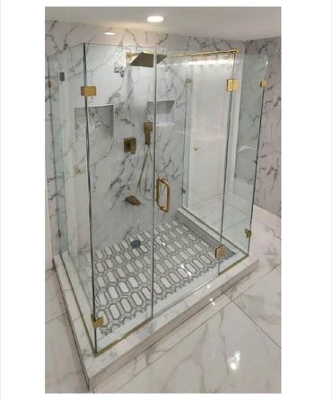 Modern glass shower enclosure with gold fixtures and patterned floor tiles.