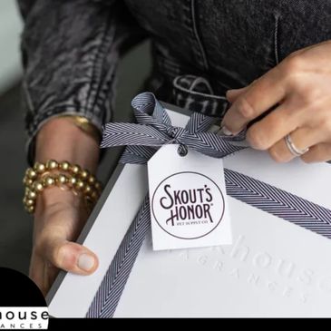 Person holding a gift box with a Skout's Honor tag and striped ribbon.