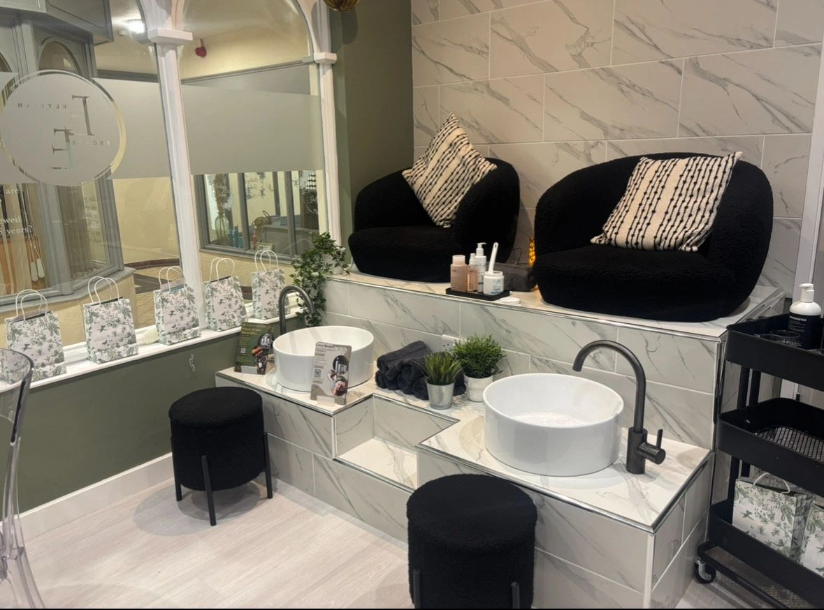 A modern pedicure station with black seats, white sinks, and decorative plants.