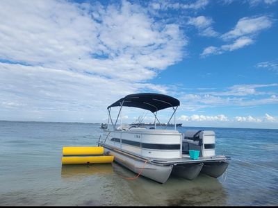 Pontoon boat docked near shore under a partly cloudy sky.