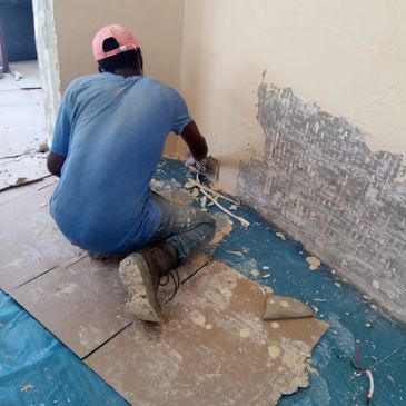 Person scraping wall plaster while kneeling on cardboard.