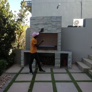 A man is inspecting a modern outdoor stone grill in a backyard.
