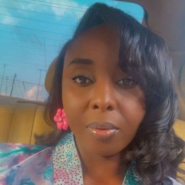 Woman with glossy lips and pink flower earrings in a car.