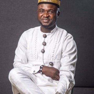 Man in traditional white attire and cap smiling.