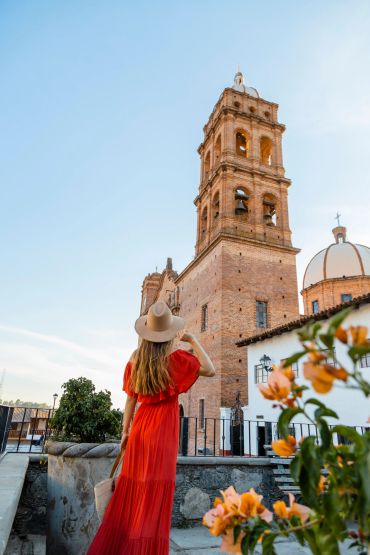 Woman in red dress admiring a historic bell tower under clear blue sky.