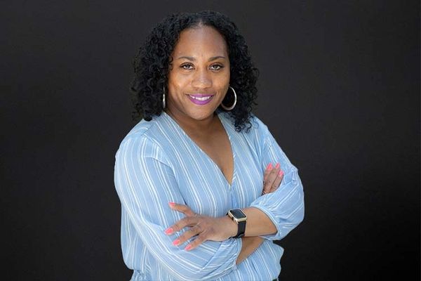 Confident woman in a striped blue shirt smiling with arms crossed.