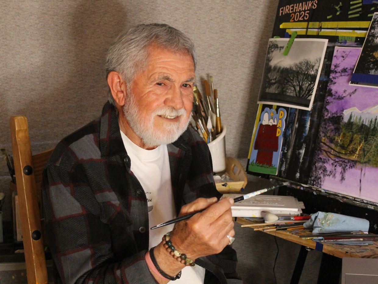 Elderly man smiling while painting in his art studio.