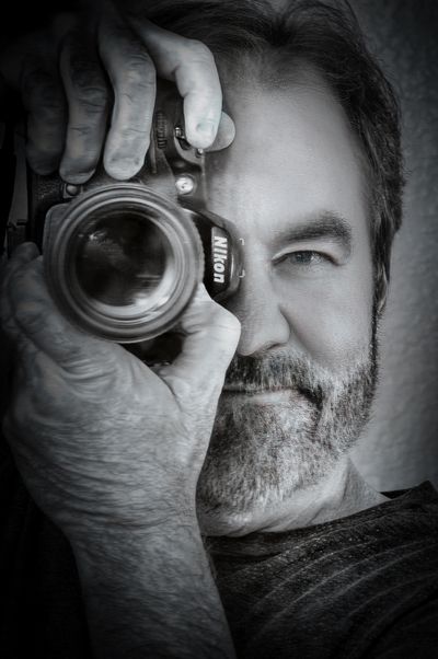 Man with a beard holding a Nikon camera up to his eye.