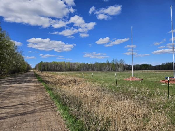 A dirt road runs alongside a grassy field under a blue sky with scattered clouds.