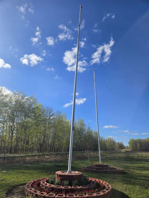 Two flagpoles without flags in a grassy area with a blue sky and scattered clouds.